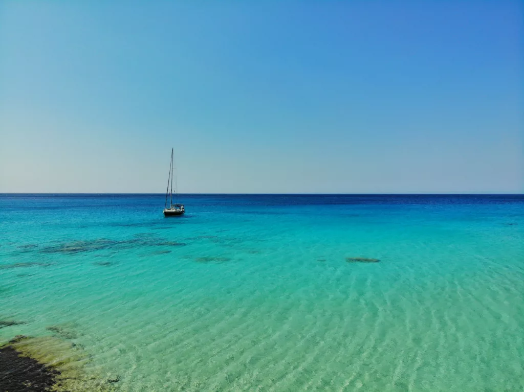 You can see Kedrodasos Beach in Pelekanos, Greece. The crystal-clear and turquoise waters make it a true sailing paradise. You might wonder is the best time to sail in Greece and when it is not too crowded like in the picture that only shows one boat and no other boat in sight