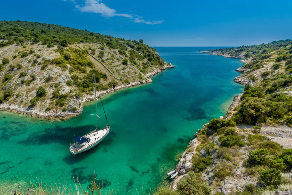 Die Umgebung um Trogir, eines der beliebtesten Segelziele in Kroatien, ist hier mit klarem blauem Himmel, türkisem Wasser und hügeliger Landschaft zu sehen