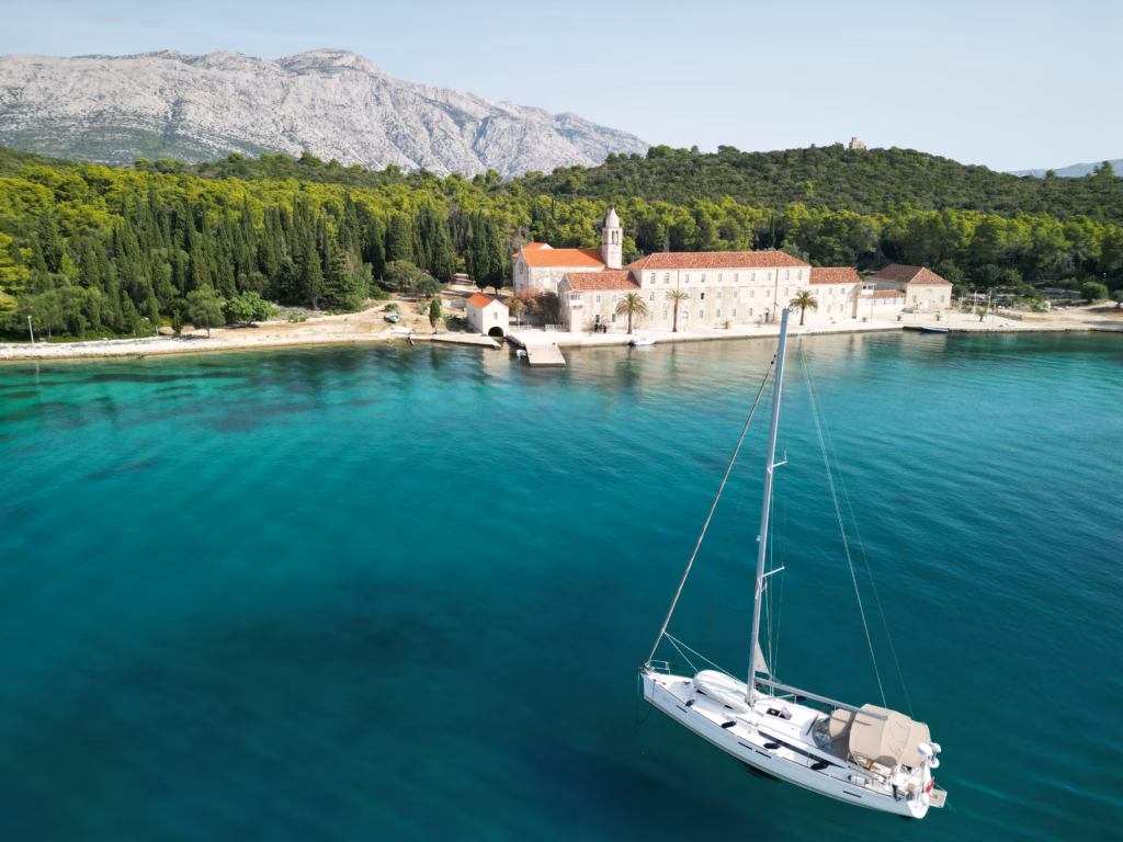 A sailboat at anchor along a Dalmatian coastline, spring light, sparse boat traffic.
